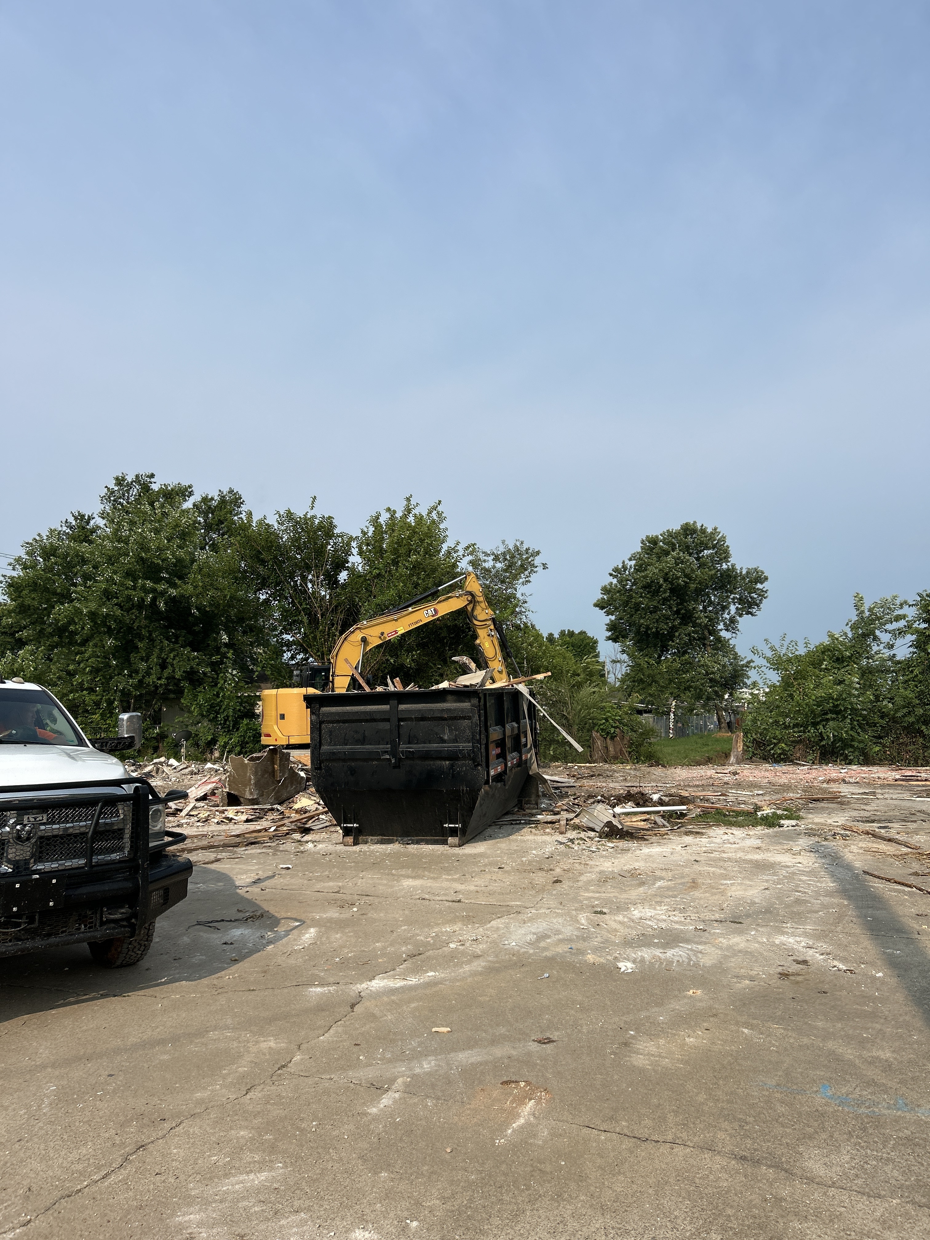 Excavator loading demolition debris into a roll-off at the Sunset and Powell project in Springdale